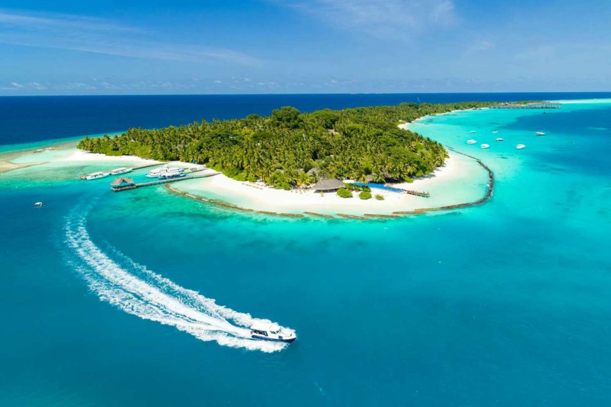 Aerial view of a Maldives resort island with a speedboat arriving